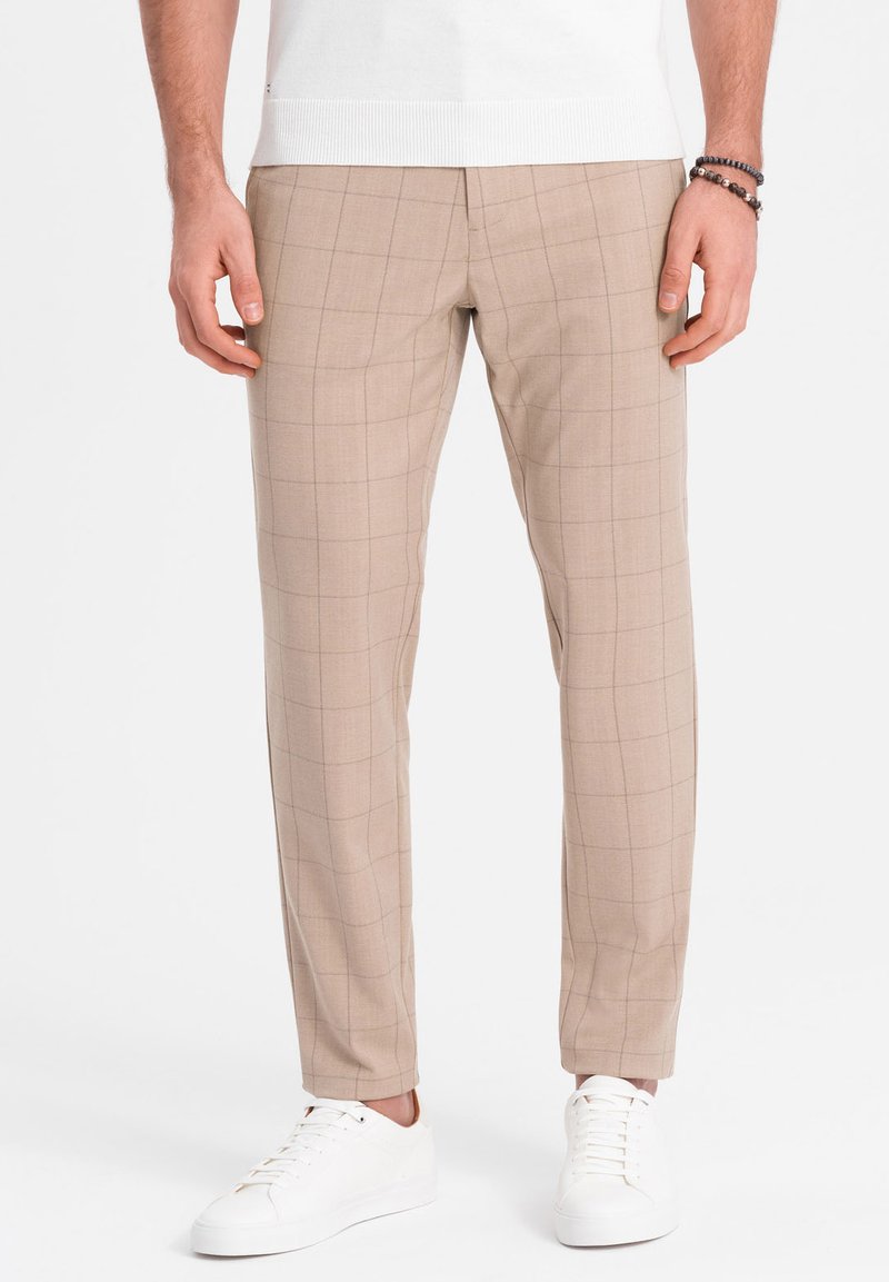 Pantalon à carreaux beiges avec une coupe ajustée, fabriqué dans un tissu lisse. Porté avec des baskets blanches, avec un design de taille standard.