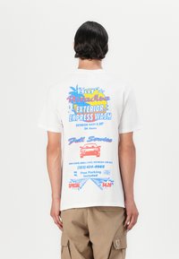 Biały bawełniany t-shirt z kolorowym nadrukiem i grafiką na plecach, w tym ilustracją samochodu i palmami. Luźny krój, krótkie rękawy.