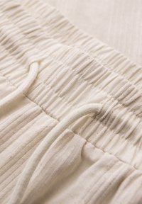Gros plan sur la ceinture d’un pantalon crème avec un élastique froncé et un cordon assorti noué à l’avant.