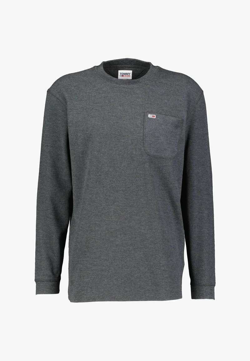 T-shirt en jersey gris à manches longues, avec un col rond, une poche poitrine et un petit logo sur la poche. Texture de tissu douce.