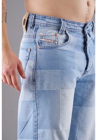 Patchwork-Jeans aus Denim in hellblauen Farbtönen mit kupferfarbenen Beschlägen, ausgestattet mit einer Vordertasche und einem Markenetikett am Taillenbund.