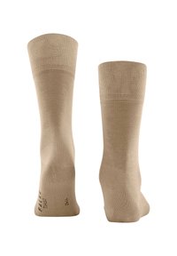 Calzini beige con un polsino a coste e una texture liscia. Presentano un marchio discreto sul lato. Modelliati per adattarsi al contorno del piede.