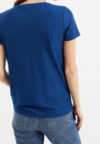 Královsky modrý top s krátkým rukávem, texturovaným vzorem, kulatým výstřihem a volným střihem, kombinovaný s džíny.