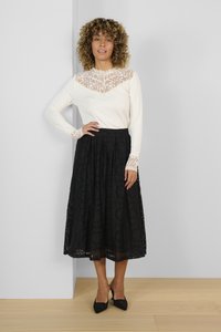 Vit långärmad topp med spetsdetaljer vid halsringningen och ärmsluten, tillsammans med en svart spets midi kjol. Svarta spetsiga klackskor fulländar outfiten.
