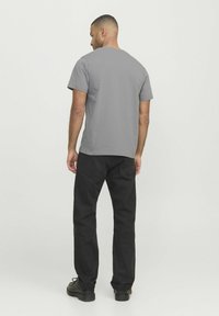 Camiseta gris de manga corta con cuello redondo, combinada con pantalones negros de pierna recta y zapatos negros, vista desde la parte trasera.