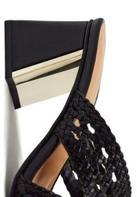 Zapato de tacón cuña negro con material trenzado, parte superior de cuero suave y detalles metálicos dorados en el tacón.