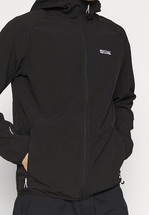 Mężczyzna w czarnej kurtce z kapturem Regatta na zamek błyskawiczny, ręce w kieszeniach, pokazujący przednią górną część ciała i logo na rękawach.