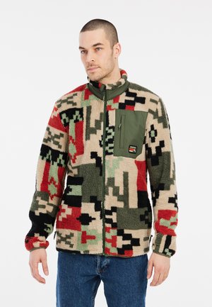 Veste en polaire dans un motif camouflage beige, noir, rouge et vert ; dotée d'une poche poitrine zippée verte et d'un col montant.