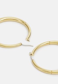 Pendientes de aro de oro con un acabado suave y brillante. Presentan un diseño tubular, un cierre de bisagra sutil y un acento plateado en el broche.