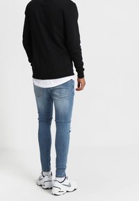 Felpa nera, jeans skinny blu con dettagli strappati e sneakers bianche con accenti neri. Design semplice e casual.