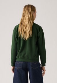 Sweatshirt vert à manches longues et ourlet côtelé, associé à un jean large bleu foncé. Texture douce, coupe décontractée et design simple.