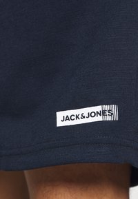 Tela azul marino con una etiqueta rectangular blanca que muestra el texto negro "JACK & JONES" y un patrón de rayas vertical cerca del dobladillo.