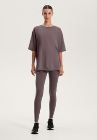 Přetékající mauve tričko s krátkými rukávy, spárované s úzkými mauve legínami. Černé sportovní boty dokreslují celý outfit.