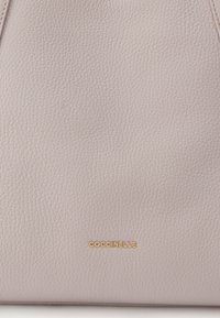 Ροζ τσάντα από δερματίνη με υφή και χρυσό λογότυπο, με μινιμαλιστικό σχεδιασμό και απαλή καμπύλωση. Η λεία επιφάνεια ενισχύει την αφής ευχάριστη αίσθηση.