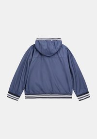 Giacca a vento blu navy con cappuccio, caratterizzata da polsini e orlo a righe bianche e blu navy, realizzata in materiale liscio e leggero.