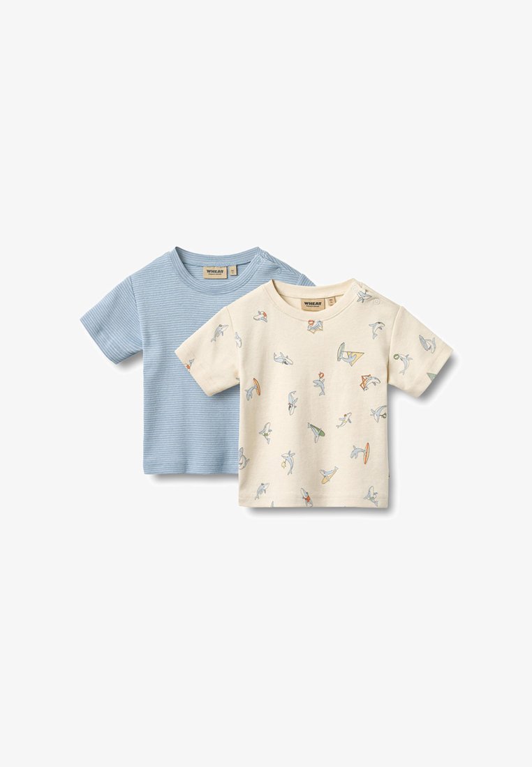 Deux t-shirts pour tout-petits, l'un bleu clair à fines rayures, l'autre crème avec de petites imprimés colorés de requins et de planches de surf.
