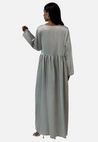 Robe longue à manches longues de couleur gris clair avec un col arrondi et une taille froncée. Tissu doux et lisse qui tombe jusqu'au sol. Design simple et élégant.