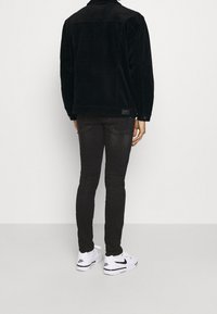 Chaqueta de terciopelo negro, silueta ajustada, con bolsillos laterales. Llevada con jeans skinny oscuros y zapatillas blancas con acentos negros.