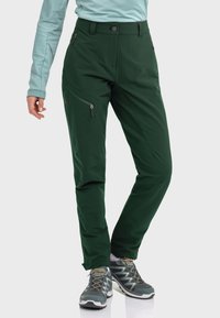 Green softshell pants with a fitted design, zippered side pockets, and a front button closure. Material appears durable and water-resistant.