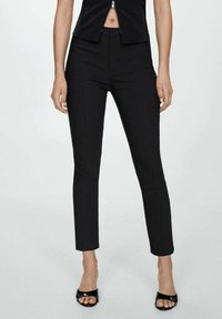 Pantaloni neri a vita alta con una vestibilità slim, caratterizzati da dettagli cucitura e una trama di tessuto liscia. Abbinati a sandali neri aperti.