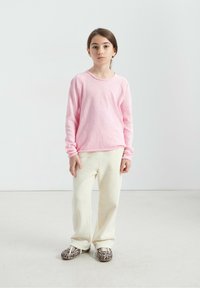 Chemise rose clair à manches longues avec un col arrondi, associée à un pantalon large crème texturé et des chaussures marron à motif léopard.