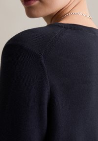 Marineblauer Strickpullover mit strukturierter Webart, rundem Ausschnitt und einem dezenten Schulterdetail. Die Rückansicht zeigt das glatte Stofffinish.