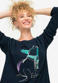 Granatowa koszula z długim rękawem, uszyta z miękkiego materiału, z abstrakcyjną grafiką w zielonym, fioletowym i białym na przodzie, luźny krój z szerokim dekoltem.