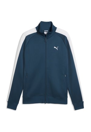 Giacca da allenamento Puma blu navy con strisce bianche sulle maniche, zip frontale completa, tasche laterali con cerniera e logo Puma sul petto.