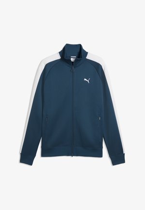 Granatowa kurtka sportowa Puma z białymi paskami na rękawach, pełnym zamkiem błyskawicznym z przodu, kieszeniami zapinanymi na zamek po bokach oraz logo Puma na piersi.