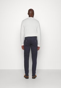 Šviesiai pilkas megztinis, tamsiai mėlyni džinsai ir rudi batai. Megztinis turi apvalų iškirpimą, o džinsai pasižymi dviem atvirais kišenėmis gale su matomu siuvimu.