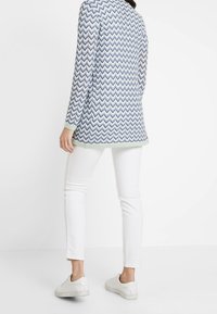 Modrý a bílý dlouhý rukáv s cikcak vzorem, vrstvený přes bílé slim-fit kalhoty, s bílými teniskami. Světle zelený akcent na spodním lemu.