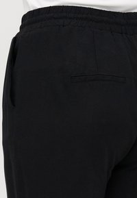 Pantalons noirs avec une taille élastique, des poches latérales et une poche arrière unique avec une finition soignée. Le tissu semble doux et léger.