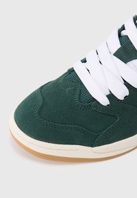 Zielone zamszowe sneakersy z białymi sznurówkami, teksturowaną powierzchnią i gumową podeszwą. Posiadają siateczkową wstawkę zapewniającą wentylację.