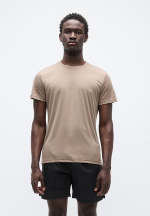 Beżowa sportowa koszulka z krótkim rękawem, wykonana z gładkiego materiału. Posiada okrągły dekolt oraz delikatną wzorzystą teksturę.