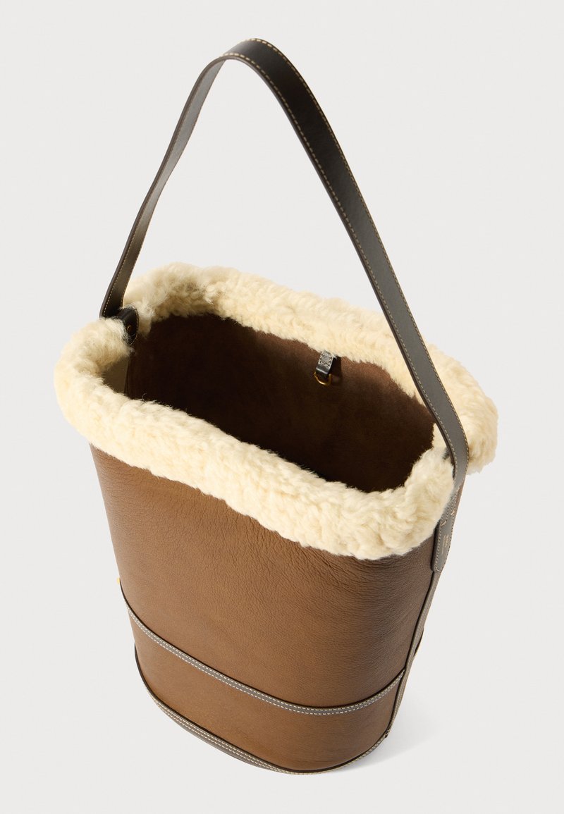 Borsa a secchiello in pelle marrone con un comfortevole rivestimento in shearling crema, un bordo superiore e una tracolla in pelle scura.