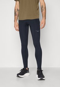 Navy athletic leggings with a fitted design, smooth texture, and a small gray logo on the left thigh. Paired with black running shoes.