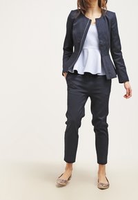 Marynarka o fakturze w kolorze granatowym z zamkiem z przodu, połączona z jasnoniebieskim topem peplum i dopasowanymi granatowymi spodniami zwężanymi ku dołowi. Do tego baleriny w nadruk.