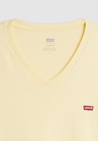 Tricou galben din bumbac cu decolteu în V, având un mic logo roșu Levi's pe partea stângă a pieptului. Textură moale și stil casual.