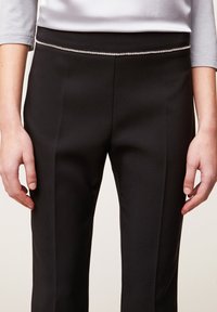 Svarta byxor med en slät textur, med en figursydd design och en dekorativ silverdetalj längs midjebandet.