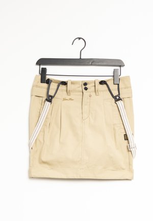 Khaki skirt with pleats, featuring a button and hook closure, adjustable gray suspender straps, and a fabric label on the side.