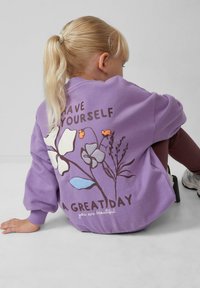 Felpa viola con grafiche floreali in bianco, arancione e blu, con la scritta "Fai in modo di avere una grande giornata" sul retro.