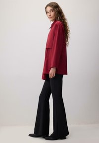 Pikkade varrukatega punane särk kihilise disainiga, kraega ja lõdva lõikega. Kandes mustade pööratud pükstega ja mustade kingadega.