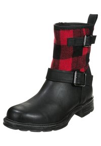 Botín de tobillo de cuero sintético negro con un eje textil a cuadros rojos y negros. Presenta dos hebillas laterales y un tacón bajo apilado.