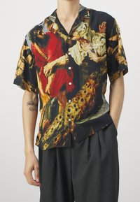 Camisa de manga corta con una vibrante obra de arte en tonos rojos, negros y dorados, elaborada con una tela ligera, con un ajuste relajado y cierre de botones.