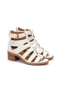 Sandalias de tacón blanco de cuero con múltiples correas, diseño de punta cuadrada, un tacón de bloque de madera y forro interior marrón. Incluye un detalle de hebilla plateada.