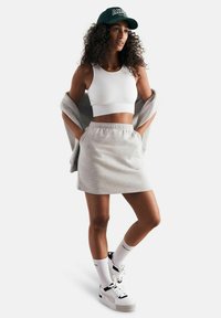 Top crop bianco a righe, gonna grigia da tuta, cardigan grigio appoggiato sulle spalle, cappellino da baseball verde, sneakers bianche con accentuazioni nere.