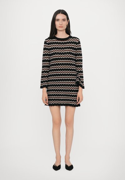Robe tricotée noire avec un motif en zigzag en crème et rose. Dotée de manches longues et d'un ourlet festonné. Associée à des ballerines noires à bout pointu.