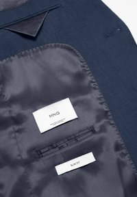Unutrašnjost mornarskog sakoa, sa satenskim oblaganjem, oznakama "MNG" i "SLIM FIT", te džepom s elegantnim dizajnom.
