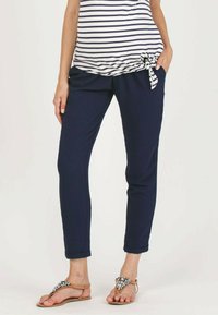 Marineblauwe broek met een ontspannen pasvorm, voorzien van een elastische tailleband en zijzakken. Gecombineerd met een gestreept shirt en platte sandalen.