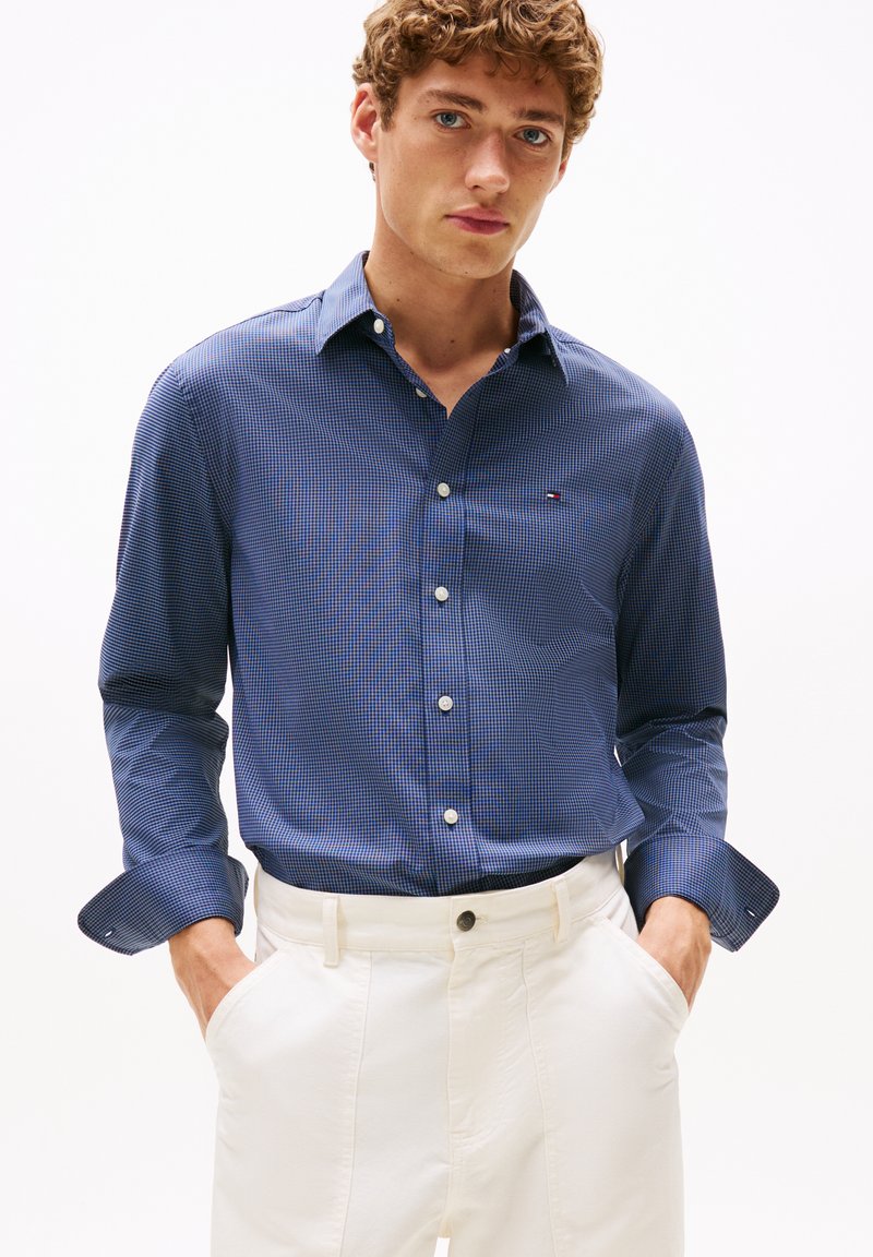 Blauw-witte geblokte shirt van katoen, met een button-down kraag, lange mouwen en een klein logo bij de borst. Gecombineerd met witte broek.